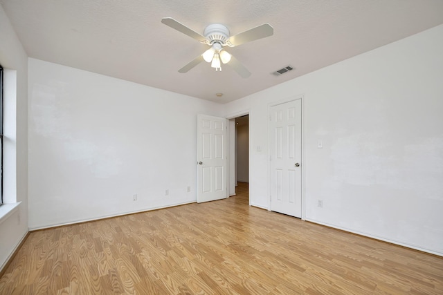 empty room featuring ceiling fan, visible vents, baseboards, and light wood-style flooring