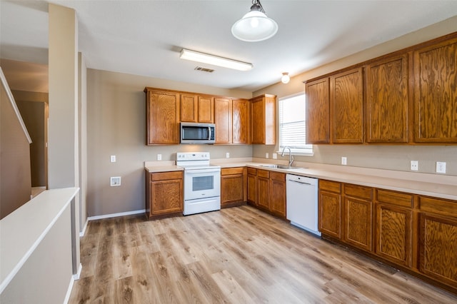 kitchen featuring light wood finished floors, a sink, white appliances, brown cabinetry, and light countertops