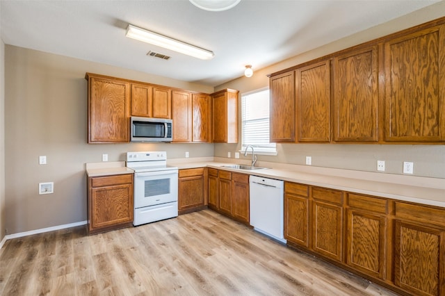 kitchen with visible vents, brown cabinets, a sink, white appliances, and light wood finished floors