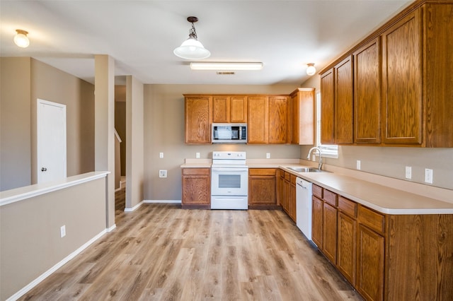 kitchen featuring light wood finished floors, a sink, white appliances, brown cabinetry, and light countertops