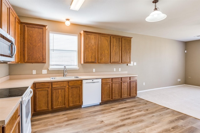 kitchen with a sink, white appliances, brown cabinets, and light wood-style flooring