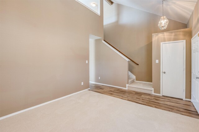 carpeted entryway with high vaulted ceiling, wood finished floors, an inviting chandelier, baseboards, and stairs