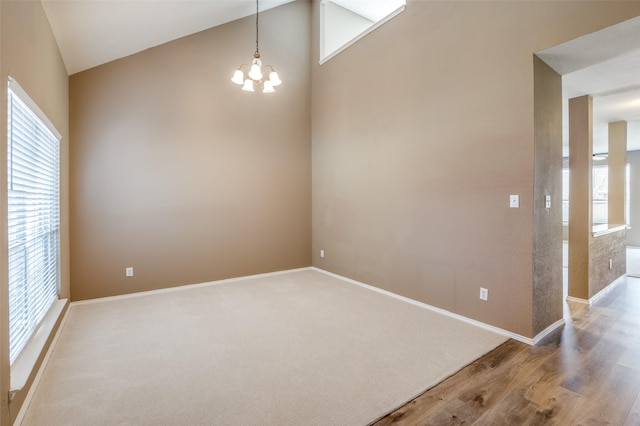 empty room with light carpet, a notable chandelier, baseboards, and high vaulted ceiling