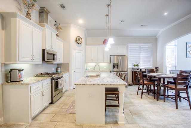 kitchen with a sink, backsplash, a breakfast bar, stainless steel appliances, and a kitchen island with sink