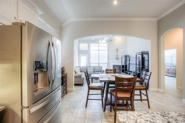 dining room with a ceiling fan, baseboards, arched walkways, ornamental molding, and a glass covered fireplace