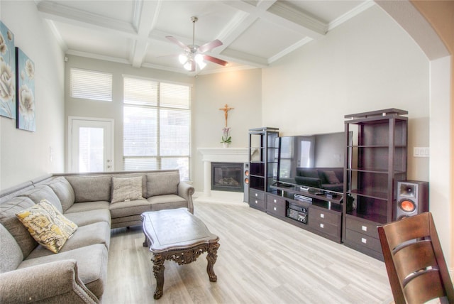 living room featuring beam ceiling, coffered ceiling, a glass covered fireplace, wood finished floors, and arched walkways