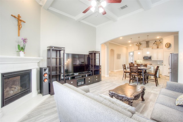 living area with visible vents, arched walkways, ceiling fan, a glass covered fireplace, and beamed ceiling