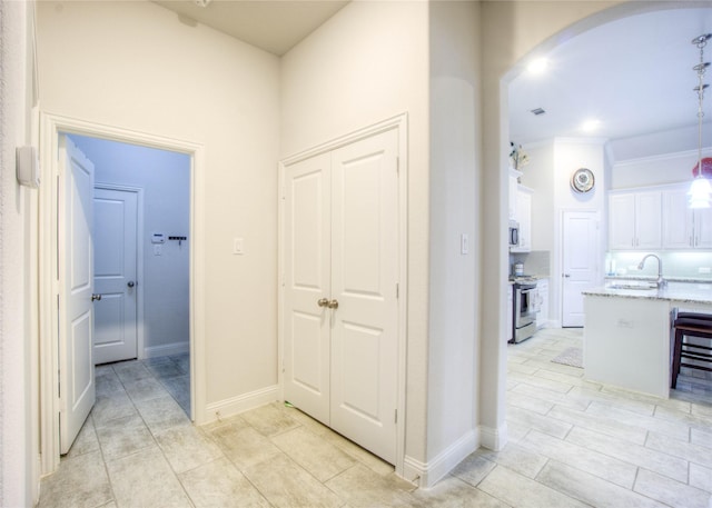 hallway featuring visible vents, a sink, arched walkways, crown molding, and baseboards