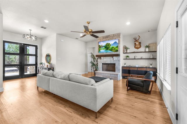 living area featuring visible vents, ceiling fan with notable chandelier, a stone fireplace, and light wood finished floors