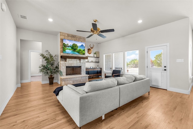 living area featuring a stone fireplace, light wood-style floors, visible vents, and ceiling fan