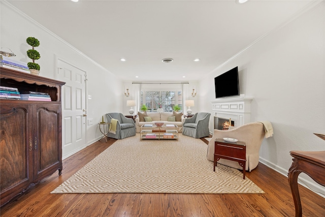 living room with crown molding, wood finished floors, visible vents, and a lit fireplace