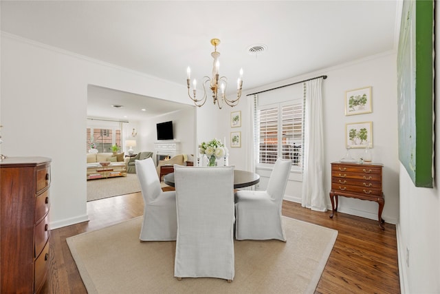 dining area with visible vents, dark wood-type flooring, ornamental molding, a lit fireplace, and an inviting chandelier