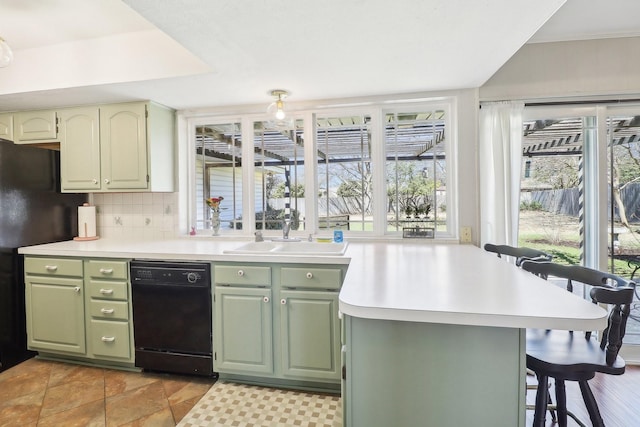 kitchen with a kitchen bar, black appliances, a sink, green cabinets, and light countertops