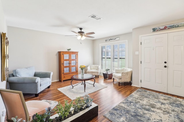 living room with ceiling fan, visible vents, baseboards, and wood finished floors