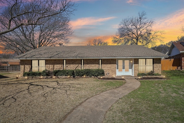 view of front of house featuring brick siding, a front lawn, fence, roof with shingles, and french doors