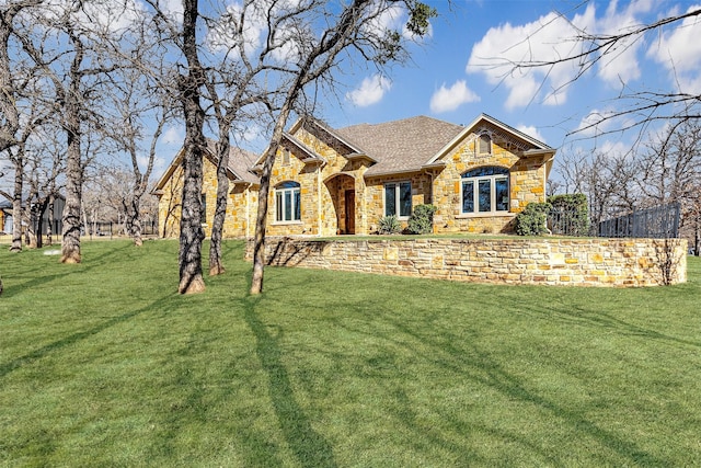 view of front of house featuring stone siding, roof with shingles, and a front yard