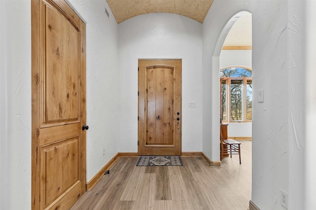 foyer entrance featuring lofted ceiling, arched walkways, baseboards, and light wood finished floors