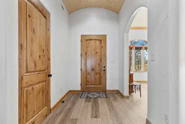 foyer entrance with arched walkways, baseboards, vaulted ceiling, and light wood-type flooring