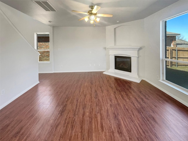 unfurnished living room featuring wood finished floors, baseboards, plenty of natural light, and a glass covered fireplace