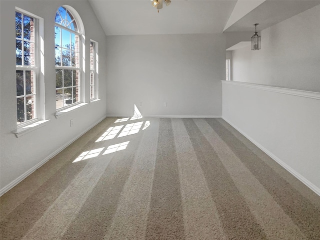 carpeted spare room featuring lofted ceiling and baseboards