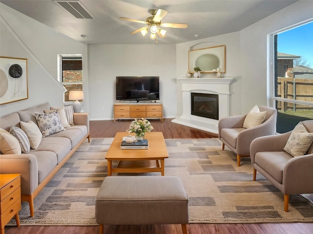 living room featuring a glass covered fireplace, visible vents, a ceiling fan, and wood finished floors