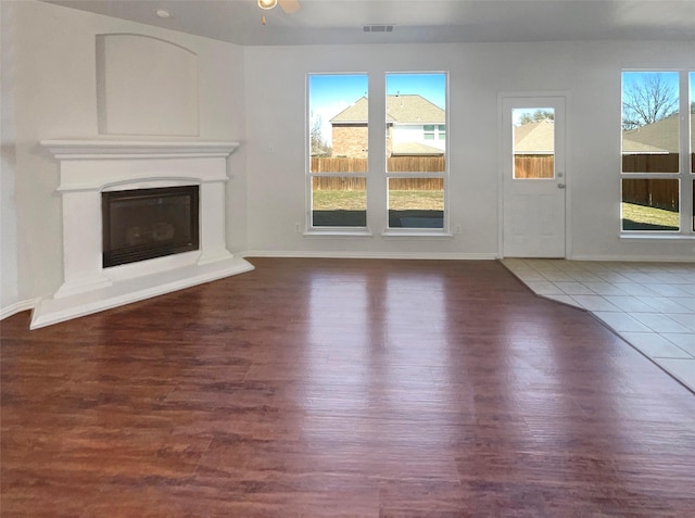 unfurnished living room featuring a glass covered fireplace, baseboards, visible vents, and wood finished floors