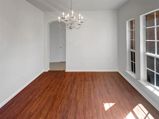 unfurnished room featuring baseboards, arched walkways, a notable chandelier, and wood finished floors