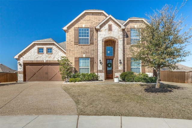 traditional-style home featuring stone siding, fence, concrete driveway, an attached garage, and brick siding