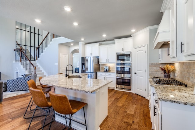 kitchen with custom range hood, a sink, wood finished floors, arched walkways, and appliances with stainless steel finishes