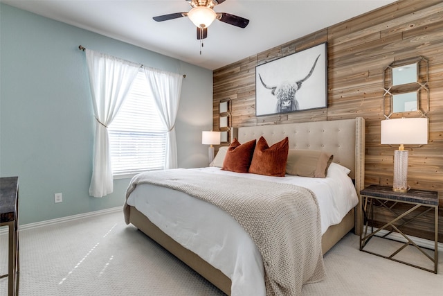 bedroom with a ceiling fan, carpet, wooden walls, baseboards, and an accent wall