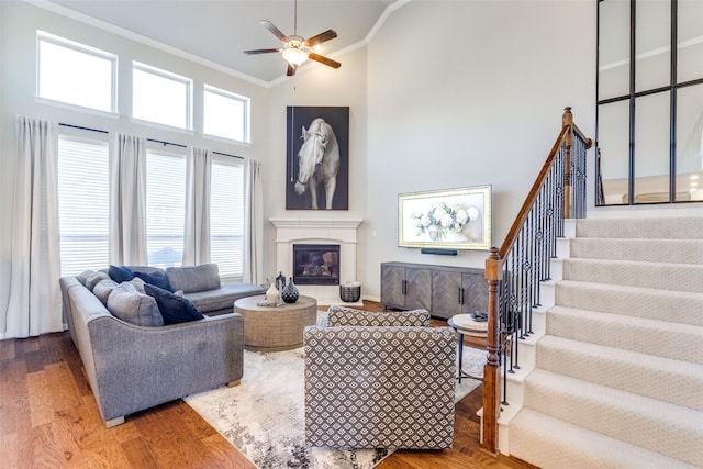 living room with high vaulted ceiling, ornamental molding, a glass covered fireplace, wood finished floors, and stairway