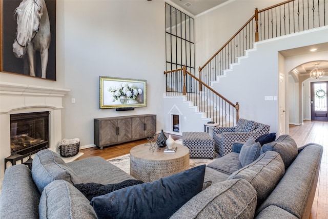 living area with wood finished floors, arched walkways, stairs, a towering ceiling, and a glass covered fireplace