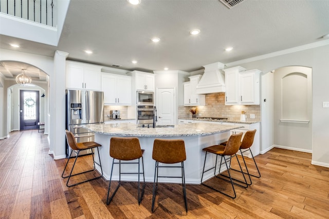 kitchen with light wood-style flooring, custom range hood, a sink, arched walkways, and appliances with stainless steel finishes