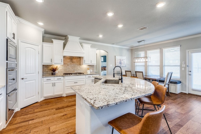 kitchen with premium range hood, a breakfast bar, arched walkways, stainless steel appliances, and a sink