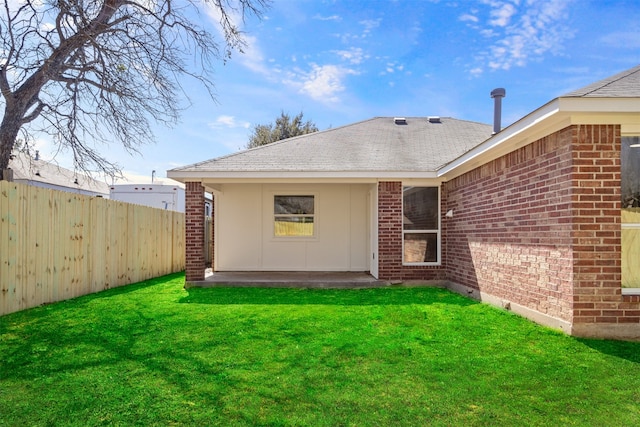 rear view of house with a yard, brick siding, a shingled roof, and fence