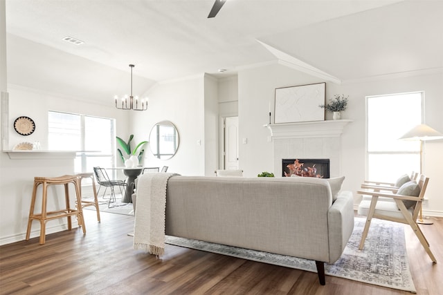 living area featuring a tiled fireplace, crown molding, wood finished floors, and visible vents