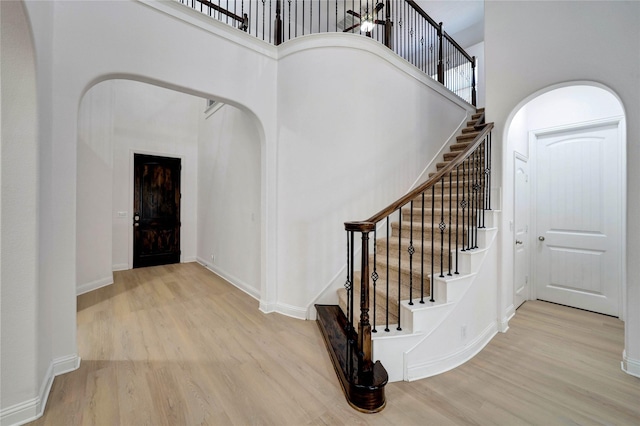 stairway with arched walkways, wood finished floors, and a towering ceiling