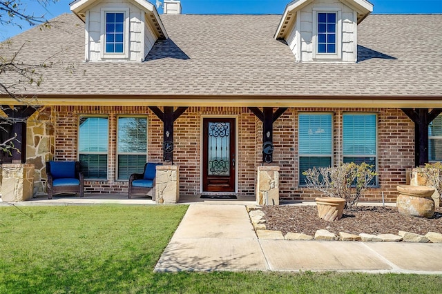 view of exterior entry featuring brick siding, a yard, and roof with shingles