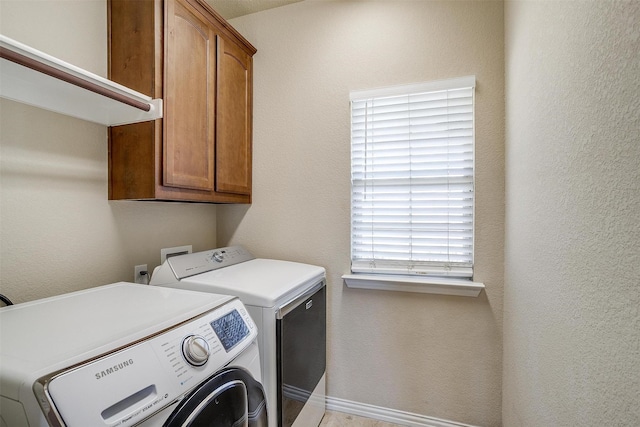 laundry area with cabinet space, baseboards, a textured wall, and washing machine and clothes dryer