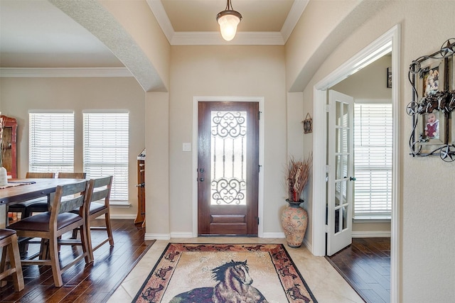 foyer featuring baseboards, arched walkways, wood finished floors, and ornamental molding