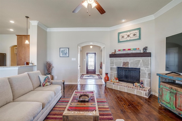 living room with baseboards, arched walkways, a stone fireplace, wood-type flooring, and crown molding