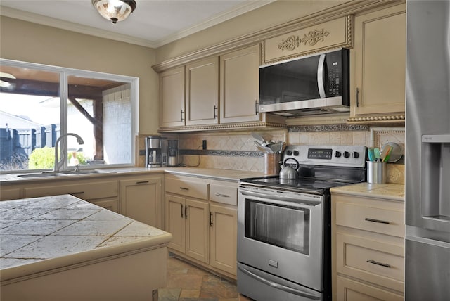 kitchen with a sink, ornamental molding, stainless steel appliances, stone finish floor, and cream cabinetry