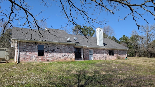 rear view of property with a yard, brick siding, roof with shingles, and a chimney