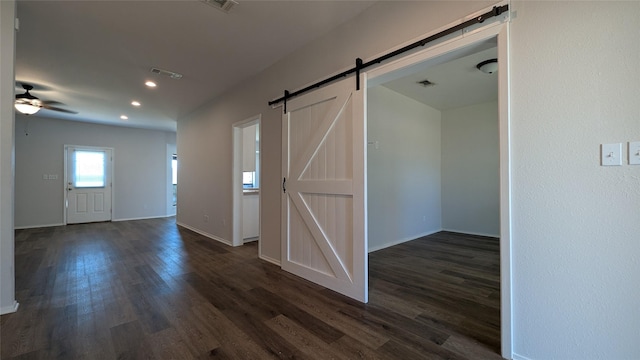 empty room with a ceiling fan, dark wood-style floors, visible vents, baseboards, and a barn door