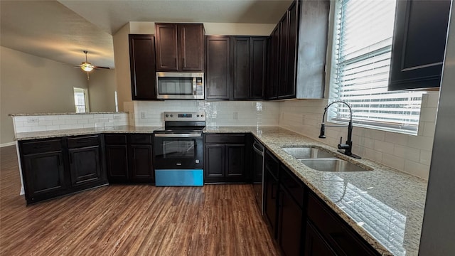 kitchen with dark wood-type flooring, a sink, stainless steel appliances, a peninsula, and light stone countertops