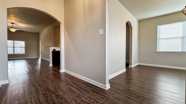 unfurnished living room with baseboards, arched walkways, dark wood-style floors, and a ceiling fan