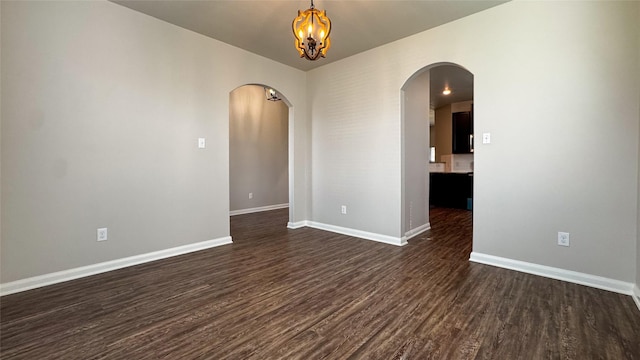 empty room with an inviting chandelier, baseboards, arched walkways, and dark wood-style flooring