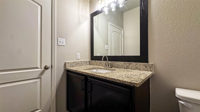 bathroom with vanity, toilet, and a textured wall