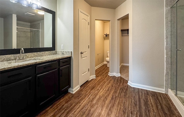 full bath featuring baseboards, toilet, a stall shower, wood finished floors, and vanity