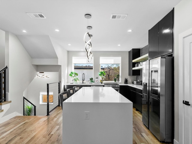 kitchen featuring visible vents, stainless steel refrigerator with ice dispenser, open shelves, a sink, and dark cabinets